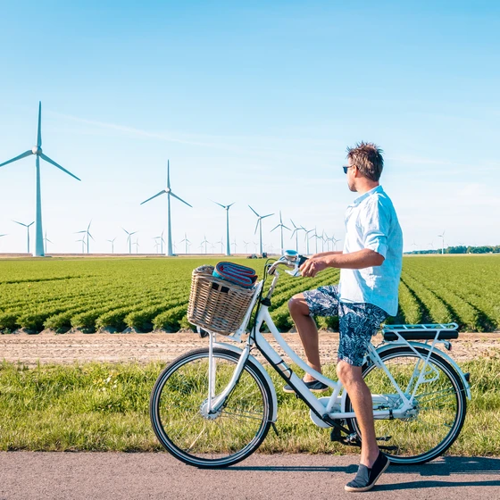 Un homme à vélo s'arrête devant un champ d’éoliennes, sous un ciel bleu clair.