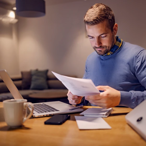 Un homme est devant son ordinateur avec des documents autour de lui.