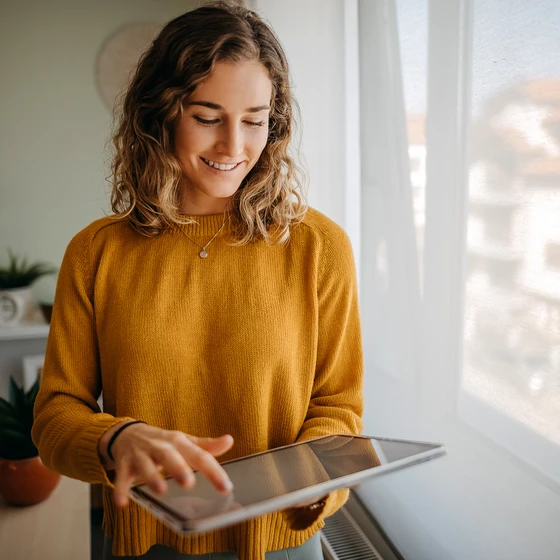 Une femme souriante consulte sa tablette pour choisir l’offre d’électricité la plus adaptée.