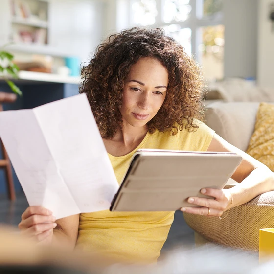 Une femme compare les offres d'électricité sur une tablette et une feuille dans un salon lumineux.