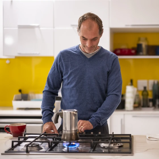 Un homme allume une cafetière sur une cuisinière à gaz dans une cuisine moderne aux tons jaunes et blancs.ancs.