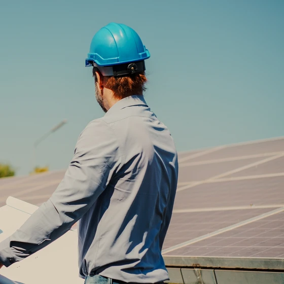 Un technicien en casque bleu observe des panneaux solaires en tenant des plans.