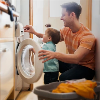 homme qui programme une machine à laver avec un enfant à côté